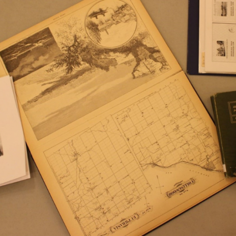 4 books spread on a beige table, only one book is seen in its entirety and shows a winter scene and a map of Collingwood Township.