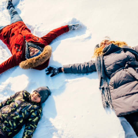 Overhead view of two adults and one child in winter clothing making snow angels