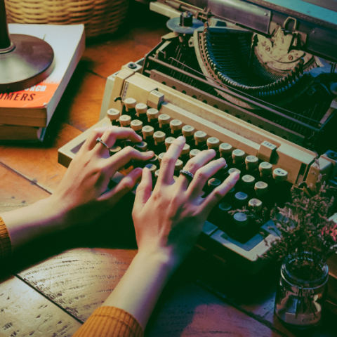 A typewriter with hands reaching from out of frame to type on it.